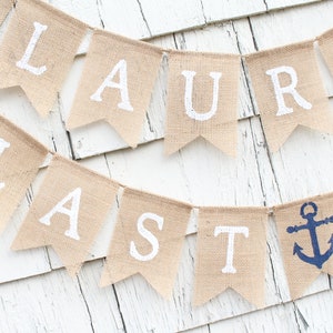 May include: A burlap banner with the words "Lauren Lasts" in white paint. The banner is decorated with two blue anchors.
