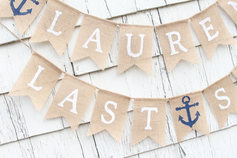 May include: A burlap banner with the words "Lauren Lasts" in white paint. The banner is decorated with two blue anchors.