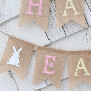 May include: A burlap banner with the words "Happy Easter" in pastel colors. The banner features a white bunny silhouette on one of the flags.