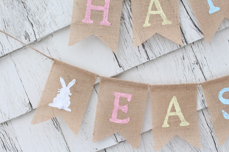 May include: A burlap banner with the words "Happy Easter" in pastel colors. The banner features a white bunny silhouette on one of the flags.