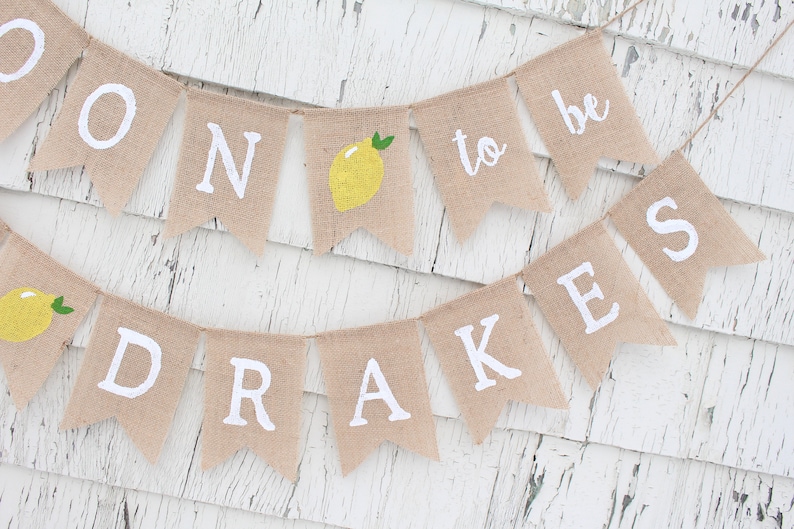 May include: A burlap banner with the words "Soon to be Drakes" in white lettering. The banner is decorated with yellow lemons and green leaves.