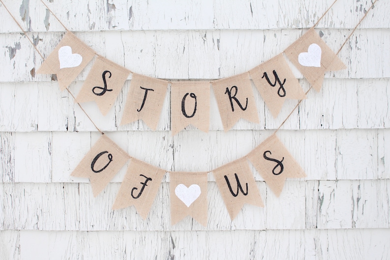 May include: A burlap banner with the words "Story of Us" in black script. The banner is decorated with white felt hearts.