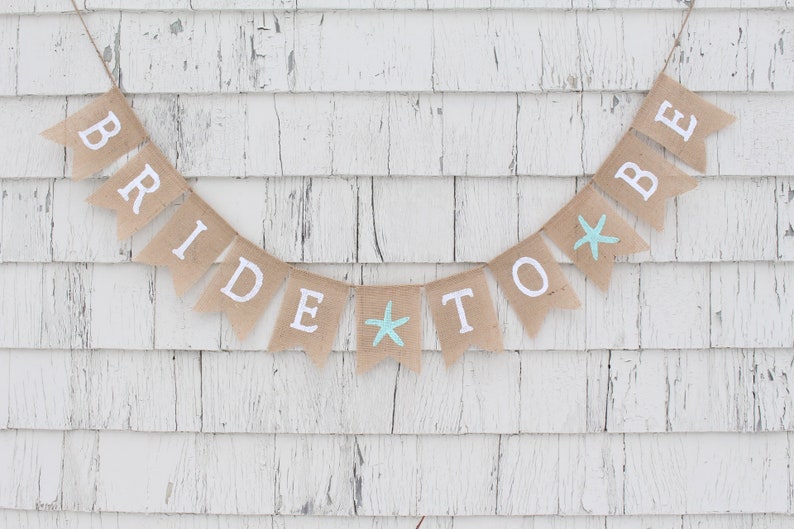 May include: A burlap banner with the words "Bride to Be" in white lettering. The banner has two blue starfish accents.