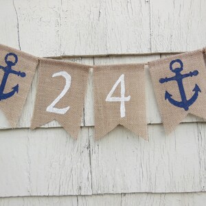 May include: A burlap banner with white numbers 24 and blue anchor symbols. The banner is strung together with twine.