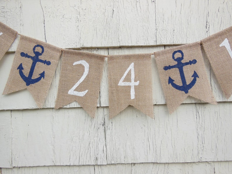 May include: A burlap banner with white numbers 24 and blue anchor symbols. The banner is strung together with twine.