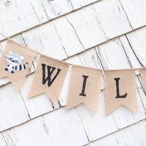 May include: A burlap banner with the word "WILD" spelled out in black letters. The banner has a small raccoon illustration on the left side.