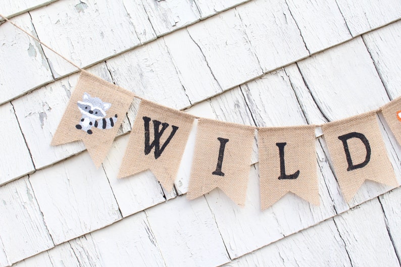 May include: A burlap banner with the word "WILD" spelled out in black letters. The banner has a small raccoon illustration on the left side.