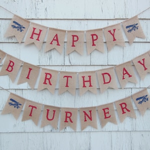 Może przedstawiać: Baner z pł&oacute;tna jutowego z czerwonymi i niebieskimi grafikami samolot&oacute;w i tekstem "Happy Birthday Turner".