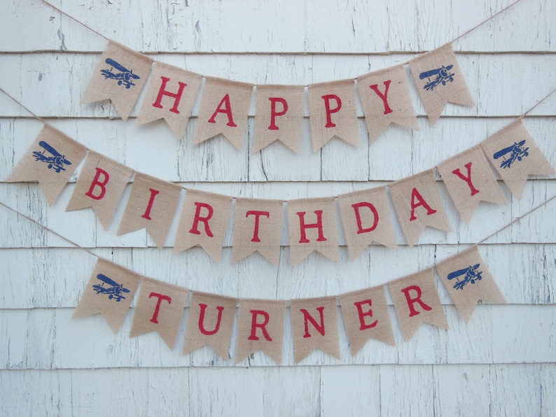 Może przedstawiać: Baner z pł&oacute;tna jutowego z czerwonymi i niebieskimi grafikami samolot&oacute;w i tekstem "Happy Birthday Turner".