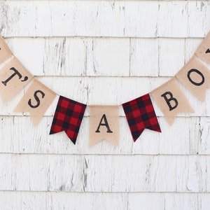 May include: A burlap banner with the words "It's a Boy" in black lettering. The banner is decorated with red and black buffalo check fabric.