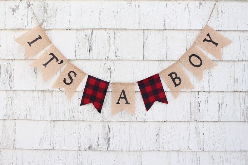 May include: A burlap banner with the words "It's a Boy" in black lettering. The banner is decorated with red and black buffalo check fabric.