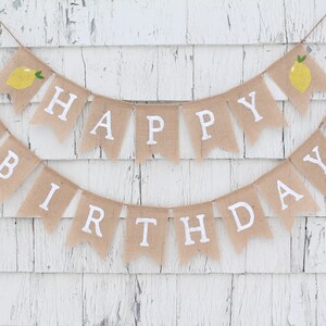 May include: A burlap banner with the words "Happy Birthday" in white letters. The banner is decorated with small yellow lemons.