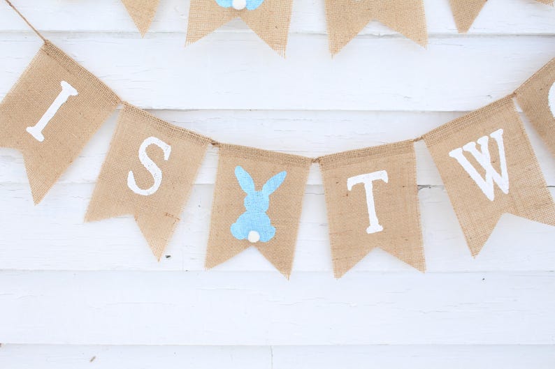 May include: A burlap banner with the words "It's Two" in white paint. A blue bunny silhouette is between the words "Two" and "It's".