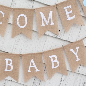May include: A burlap banner with the words "COME BABY" in white paint. The banner is strung with blue hearts.