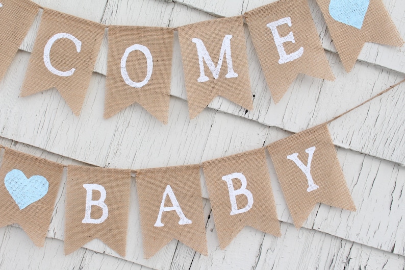 May include: A burlap banner with the words "COME BABY" in white paint. The banner is strung with blue hearts.