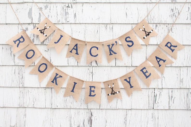 Pu&ograve; includere: Uno striscione di juta con il testo "JACK'S ROOKIE YEAR" in lettere blu scuro. Lo striscione &egrave; decorato con bastoni da hockey e dischi.