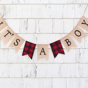 May include: A burlap banner with the words "It's a Boy" in black lettering. The banner has red and black buffalo check fabric accents.