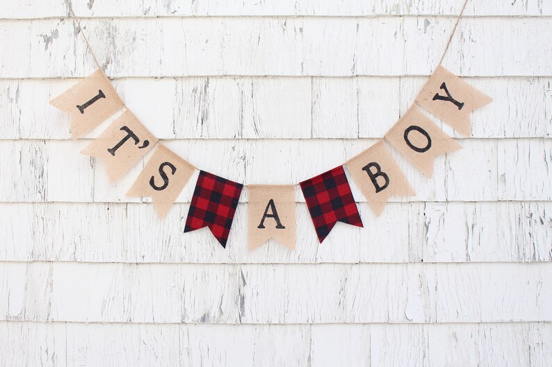May include: A burlap banner with the words "It's a Boy" in black lettering. The banner has red and black buffalo check fabric accents.