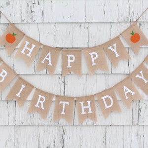 May include: A burlap banner with the words "Happy Birthday" in white letters. The banner is decorated with small orange fruit illustrations.