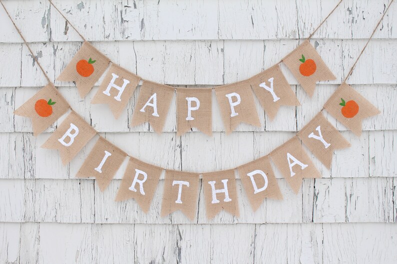 May include: A burlap banner with the words "Happy Birthday" in white letters. The banner is decorated with small orange fruit illustrations.
