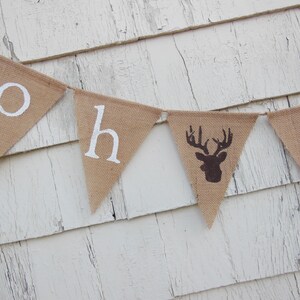 Puede incluir: Una pancarta de arpillera con las palabras "Oh Deer" pintadas en blanco. La pancarta tiene una silueta de ciervo marr&oacute;n en el centro.