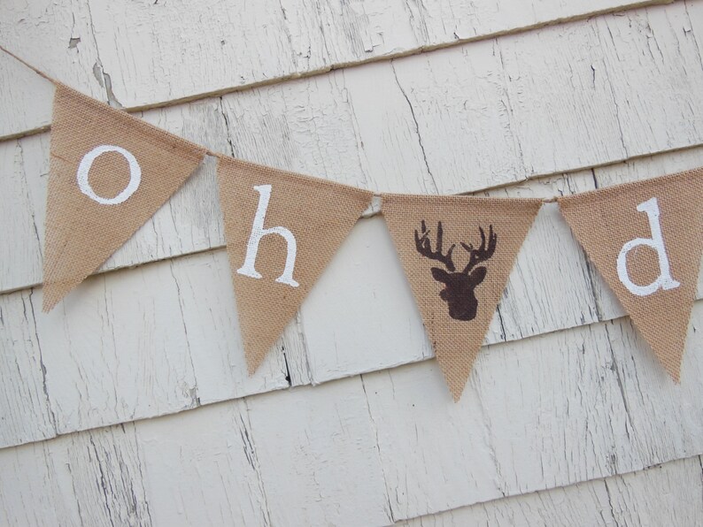 Puede incluir: Una pancarta de arpillera con las palabras "Oh Deer" pintadas en blanco. La pancarta tiene una silueta de ciervo marr&oacute;n en el centro.