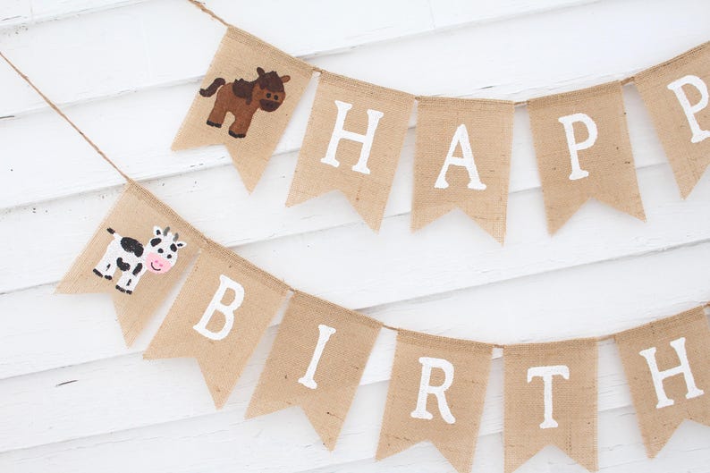 May include: A burlap banner with the words "Happy Birthday" in white paint. The banner is decorated with a brown horse and a black and white cow.
