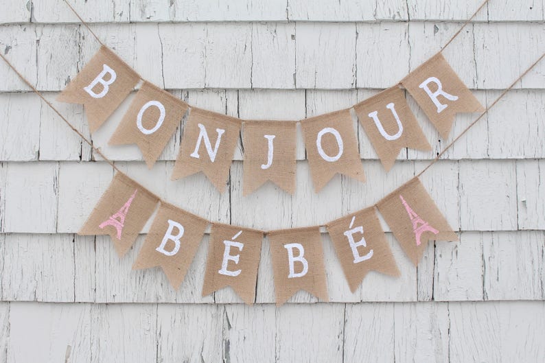 May include: A burlap banner with the words "Bonjour B&eacute;b&eacute;" in white lettering. The banner is decorated with pink Eiffel Tower symbols.