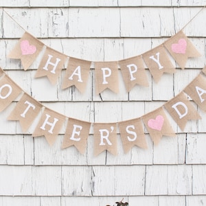 May include: A burlap banner with the words "Happy Mother's Day" in white letters. The banner has pink hearts on each end.