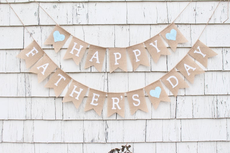 May include: A burlap banner with the words "Happy Father's Day" in white letters. The banner has three blue hearts.