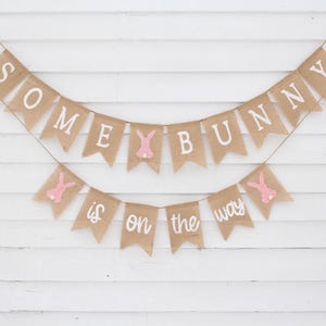 May include: A burlap banner with pink bunny cutouts and the text "Some bunny is on the way".