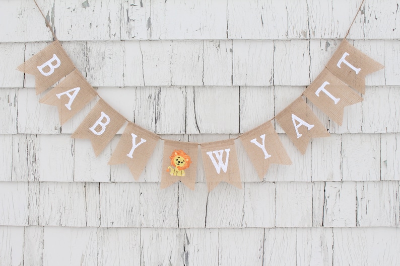 Pode incluir: Uma faixa de juta com as palavras "Baby Wyatt" em letras brancas. Uma pequena ilustra&ccedil;&atilde;o de le&atilde;o est&aacute; entre o "Y" e o "W".