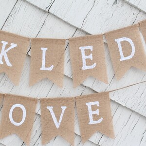 May include: A burlap banner with the words "Thank You" and "Loved" in white letters. A pink heart is on the right side of the banner.