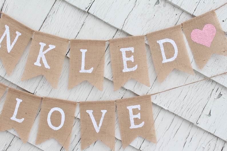 May include: A burlap banner with the words "Thank You" and "Loved" in white letters. A pink heart is on the right side of the banner.
