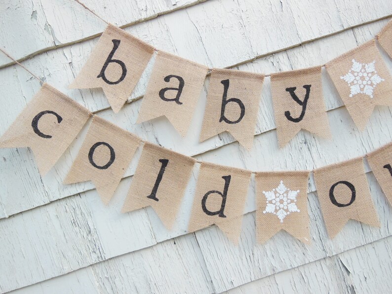 May include: A burlap banner with the words "baby cold out" in black lettering. The banner is decorated with white snowflakes.