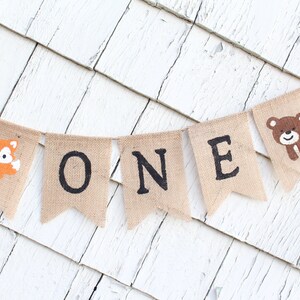 May include: A burlap banner with the word "ONE" in black letters. The banner is decorated with a fox and a bear.