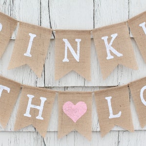 May include: A burlap banner with the words "Sprinkle with Love" in white lettering. A pink heart is in the middle of the banner.