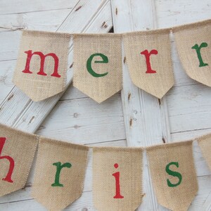 K&ouml;nnte beinhalten: Ein Wimpelbanner mit den Worten "merry christmas" in roten und gr&uuml;nen Buchstaben. Das Banner besteht aus einzelnen wimpelf&ouml;rmigen Flaggen, die aneinandergereiht sind. Der Hintergrund ist eine wei&szlig;e Holzt&uuml;r.