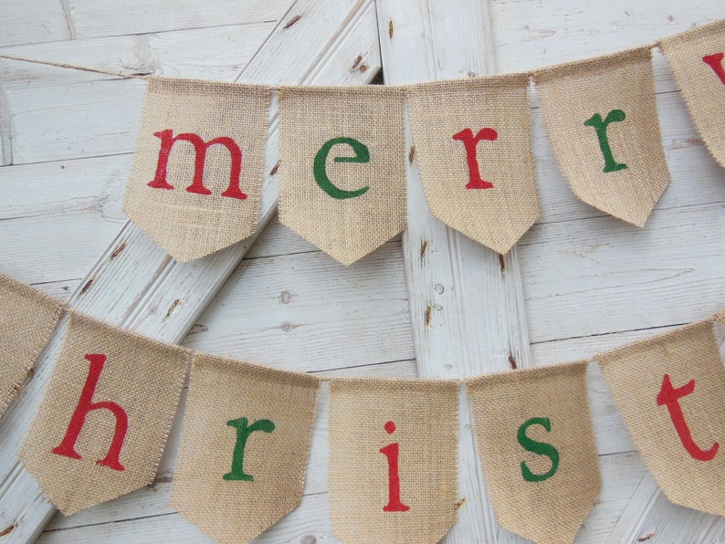 K&ouml;nnte beinhalten: Ein Wimpelbanner mit den Worten "merry christmas" in roten und gr&uuml;nen Buchstaben. Das Banner besteht aus einzelnen wimpelf&ouml;rmigen Flaggen, die aneinandergereiht sind. Der Hintergrund ist eine wei&szlig;e Holzt&uuml;r.