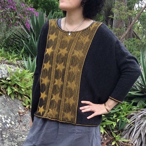 May include: A black and yellow knit sweater with a star pattern. The sweater has a wide, loose fit and a scoop neck.