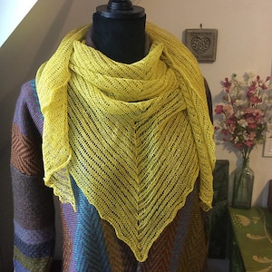 May include: A yellow knitted shawl with a lacy pattern, draped over a mannequin wearing a brown and blue patterned sweater.