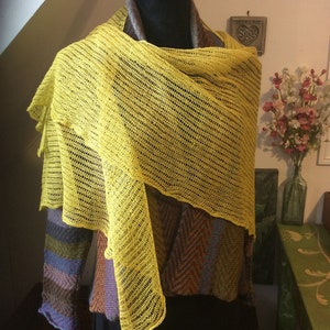 May include: A yellow knitted shawl draped over a mannequin. The shawl is made of a delicate, open-weave fabric.