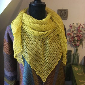 May include: A yellow knitted shawl with a lacy pattern, draped over a mannequin wearing a brown and blue patterned sweater.