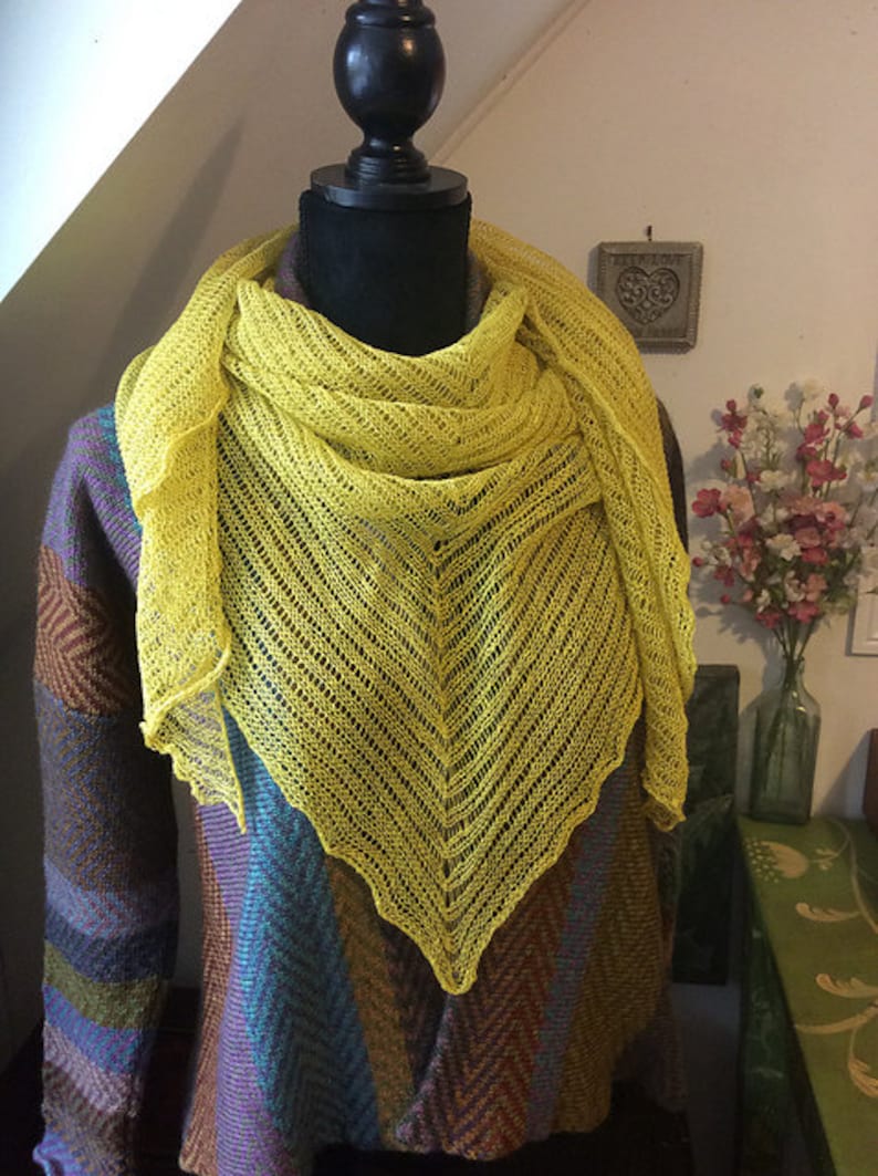 May include: A yellow knitted shawl with a lacy pattern, draped over a mannequin wearing a brown and blue patterned sweater.