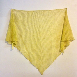 May include: A yellow crocheted shawl with a chevron pattern. The shawl is hanging on a white wall.