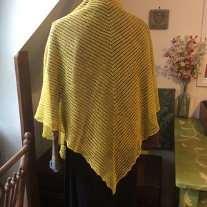 May include: A yellow crocheted shawl with a triangular shape. The shawl is made with a delicate open stitch pattern.