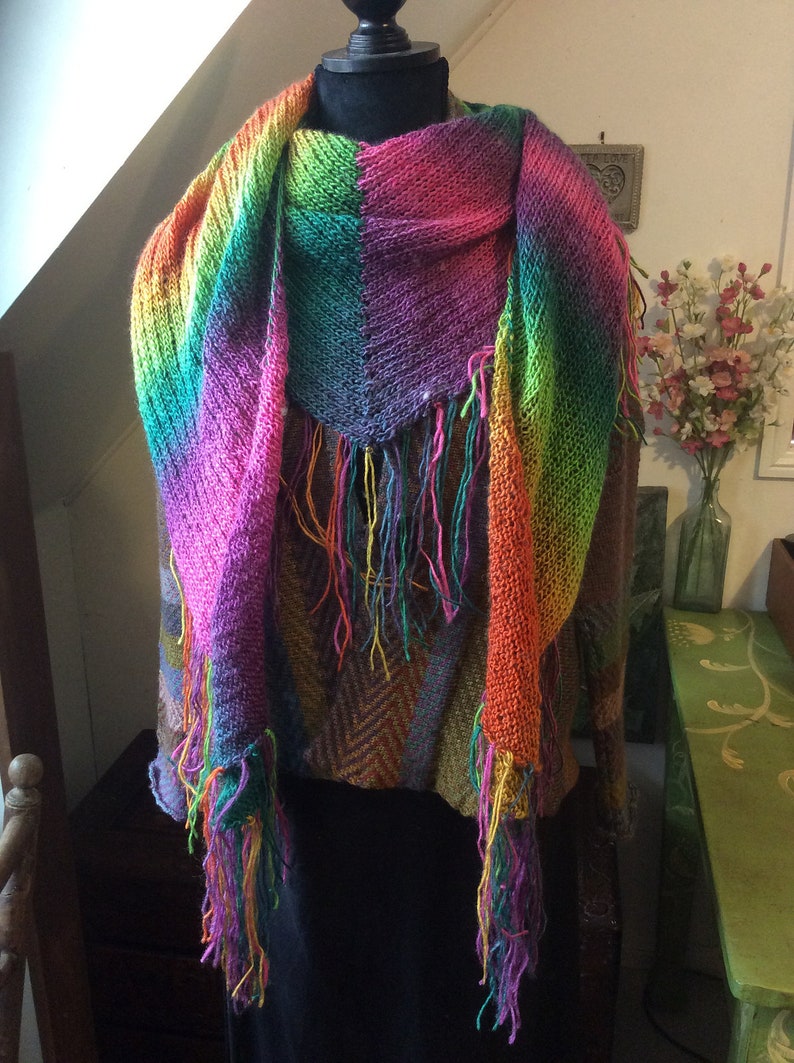 May include: A colorful knitted scarf with fringe, featuring a rainbow gradient of pink, orange, yellow, green, blue, and purple.