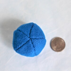 May include: A small, blue, felt ball with a diameter of about 1 inch. The ball is sewn with four seams that form a cross shape.