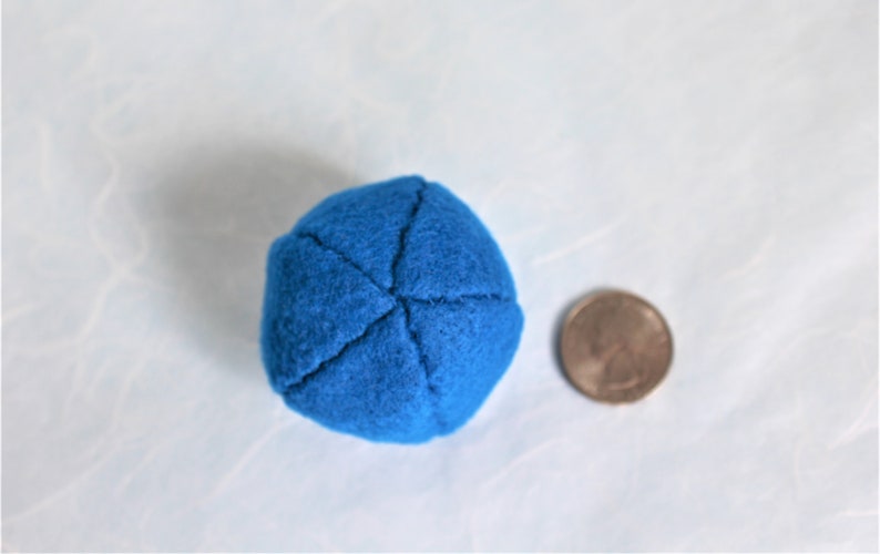 May include: A small, blue, felt ball with a diameter of about 1 inch. The ball is sewn with four seams that form a cross shape.