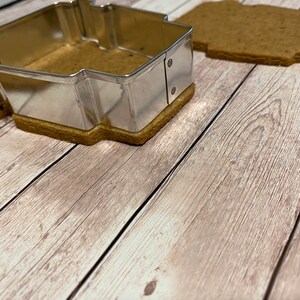 May include: A metal cookie cutter in the shape of a house, with a gingerbread cookie inside.
